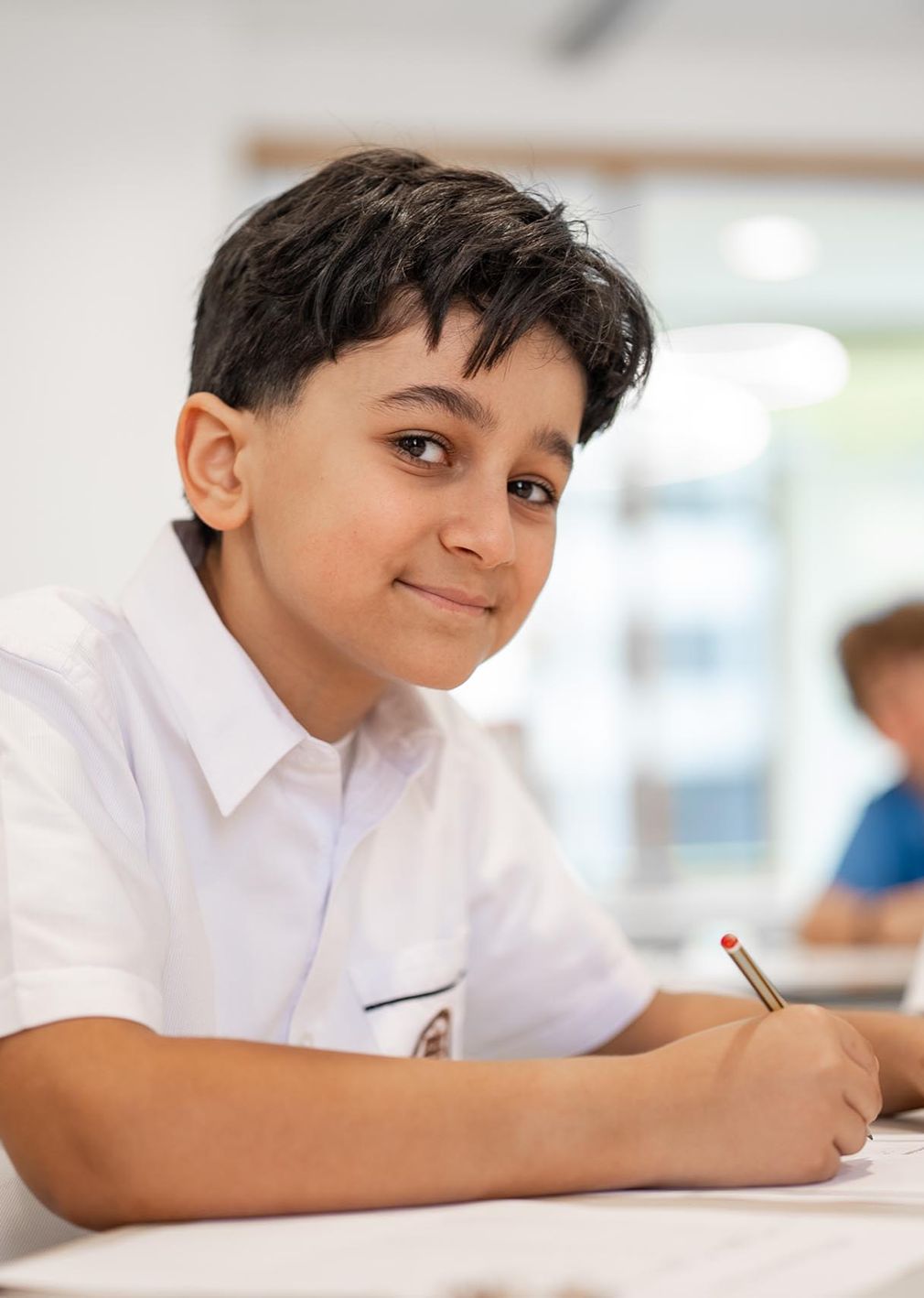 Student smiling, sitting at a desk holding a pen