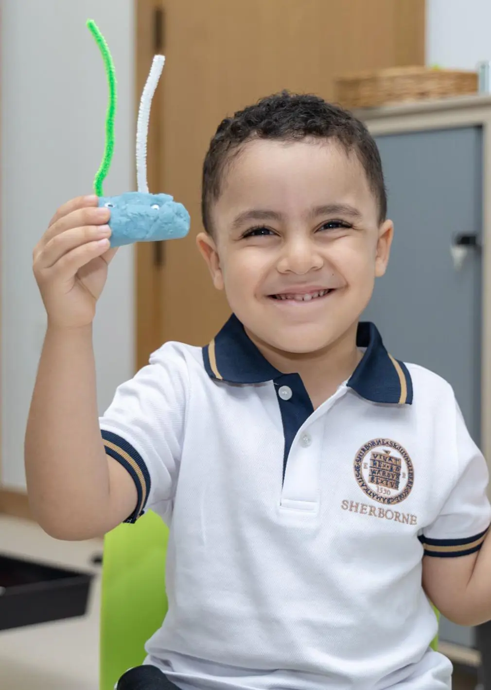 Sherborne Jeddah student holding playdough creation and smiling.