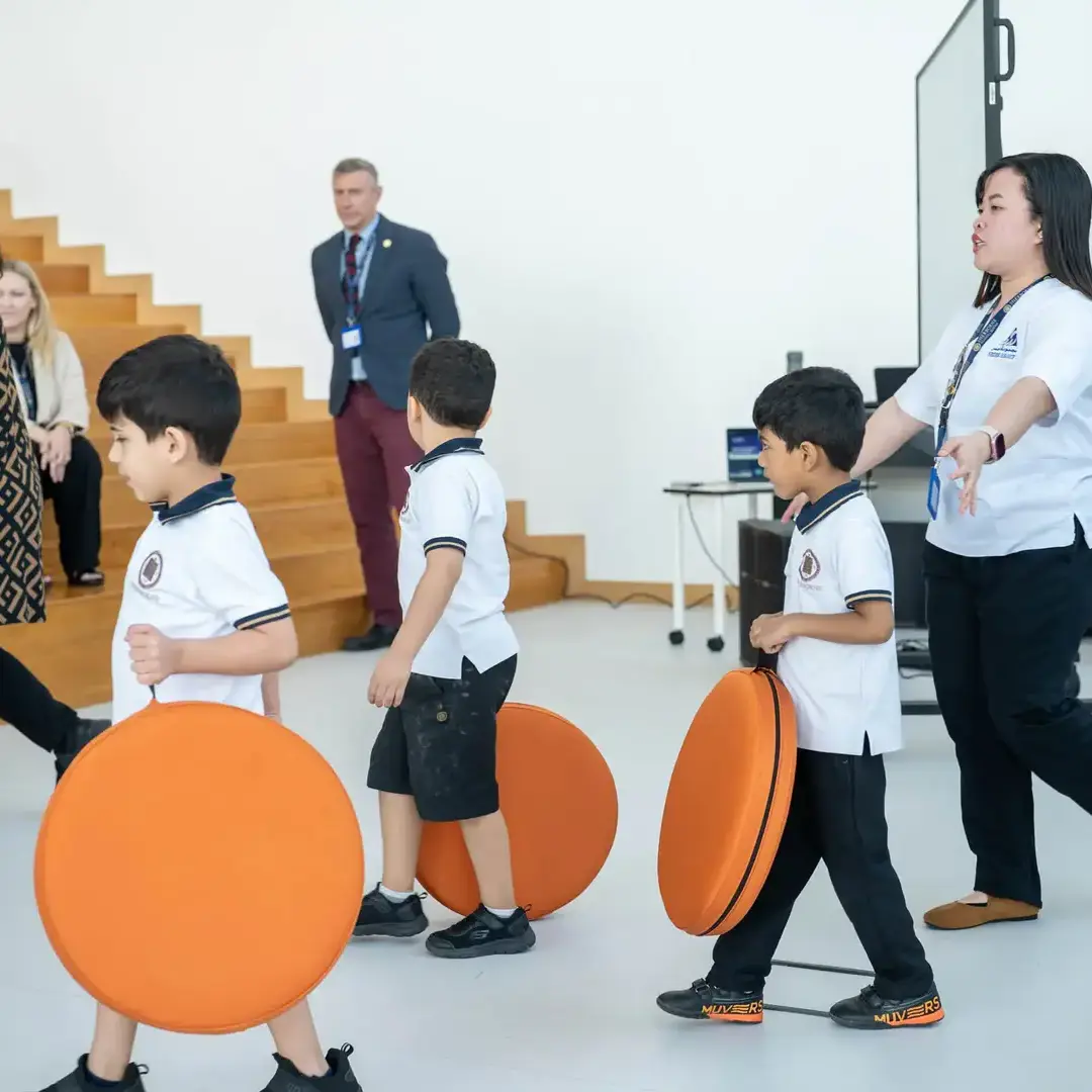 Sherborne School Jeddah students carrying cushions to benches for assembly.