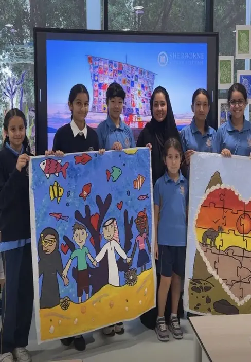 Sherborne School Jeddah students holding up their paintings for a photograph.